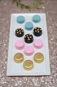 there is a white plate with different types of cookies on it and some pink, blue, and gold buttons