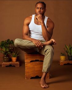 a man sitting on top of a wooden box next to potted plants and holding his chin up