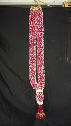 a red and white beaded necklace hanging on a black background with gold accents,