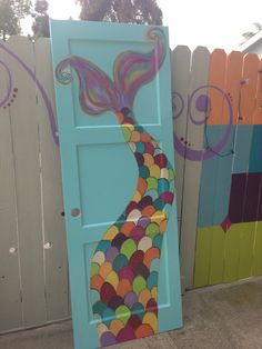 a painted door with a colorful mermaid tail on it's side in front of a fence