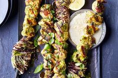 several skewers of food on a tray with dipping sauce and lemon wedges