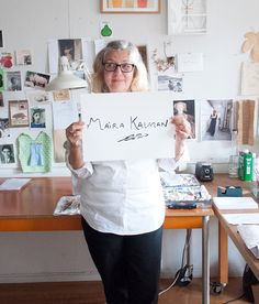 a woman holding up a sign in front of a desk with many pictures on it