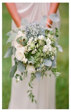 a bride holding a bouquet of white and blue flowers on her wedding day in the grass