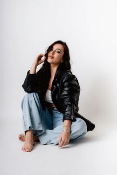 a woman sitting on the ground wearing jeans and a black jacket