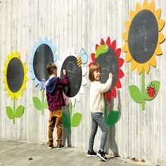 two children standing in front of a wall with flowers and chalkboards on it