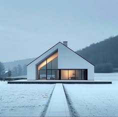 a white house sitting in the middle of a snow covered field next to a forest