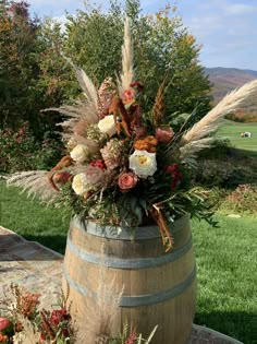 a wooden barrel filled with lots of flowers next to a lush green field and trees