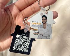 a person holding a house shaped keychain with a qr code attached to it