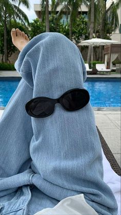 a person with sunglasses covering their face sitting in front of a pool wearing a blue towel