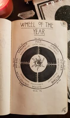 an open book with the wheel of the year written on it next to a candle