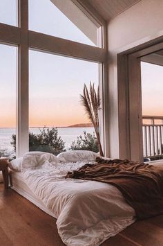 a bed sitting in front of large windows next to a wooden floor covered with white sheets