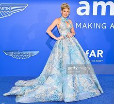 a woman in a blue and white gown poses on the blue carpet at an event