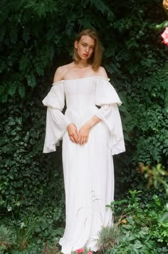 a woman in a white dress standing next to some bushes