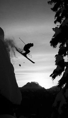 a person jumping in the air while riding skis on a snowy mountain side at sunset