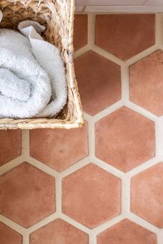 a basket with a white towel on top of it next to a tiled wall and floor