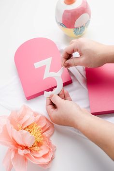 someone is cutting out the number from a heart shaped card with scissors and pink paper