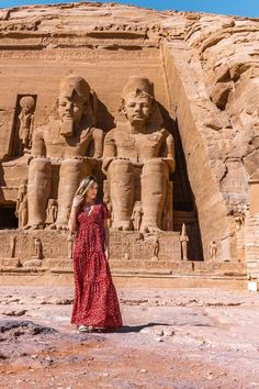 a woman in a red dress standing next to an ancient building with statues on it