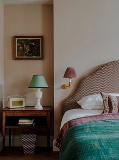 a bed sitting next to a nightstand with a lamp on top of it in a bedroom