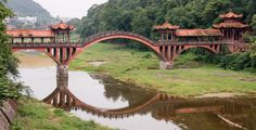 a bridge over a body of water surrounded by lush green grass and trees in the background