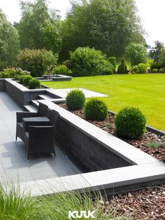 an outdoor seating area in the middle of a park with grass and bushes around it