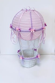 a pink and purple paper lantern in a basket on a white surface with ribbons around it