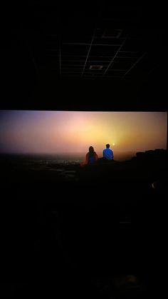 two people sitting on a bench watching the sun go down over the horizon in an open area