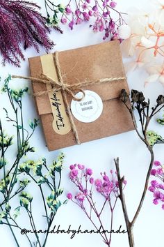 a brown envelope tied with twine and surrounded by purple flowers on a white surface