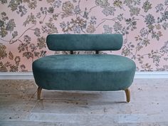 a green chair sitting in front of a pink wall with flowers on the wall behind it