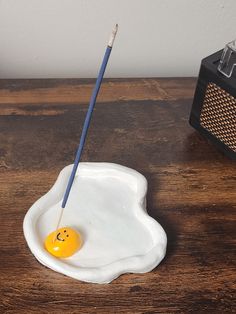 an egg shell with a smiley face painted on it and a pencil in the bowl