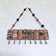 a wine cork wall hanging with metal hooks and beaded beads on the end, attached to a white wall