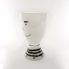 a white and black striped vase with a face drawn on the side, in front of a white background