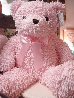 a large pink teddy bear sitting on top of a white toilet in a room next to a mirror