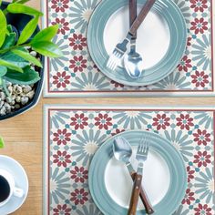 two placemats with forks and spoons on them next to a potted plant