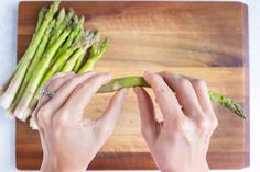 a person is cutting asparagus on a wooden board