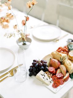 a white table topped with lots of different types of cheeses and fruit on top of it