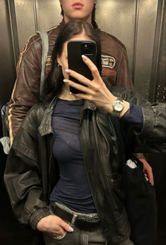 a woman taking a selfie with her cell phone in front of a man wearing a leather jacket