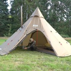 a man sitting inside of a tent on top of a lush green field