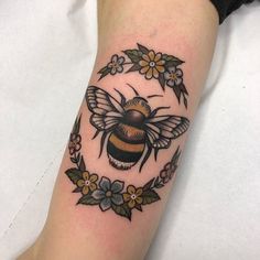 a tattoo with a bee and flowers on the arm that is sitting on a person's leg