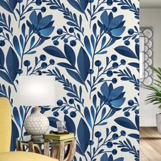 a blue and white floral wallpaper in a living room with a yellow chair, table lamp and potted plant