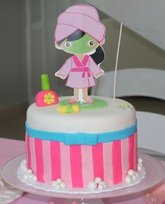 a birthday cake with a girl in a pink hat on top and decorations around it