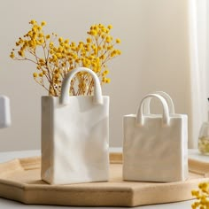 two white bags sitting on top of a wooden tray next to yellow flowers in vases