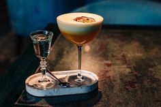 an alcoholic drink is served in a coupe glass on a tray with a wineglass