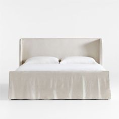 an upholstered bed with white sheets and pillows