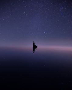 a person sitting on the edge of a body of water under a night sky filled with stars