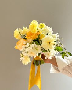 a person holding a bouquet of yellow and white flowers in their hand with a yellow ribbon around it