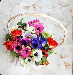 a basket filled with lots of colorful flowers on top of a white table covered in paper