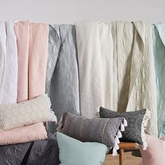 pillows and blankets lined up against a wall in front of a wooden table with a chair