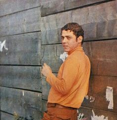 a man standing in front of a wooden wall with graffiti on it and writing on the wall