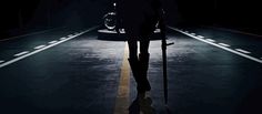 a person walking down the street at night with an umbrella over their head and a car behind them