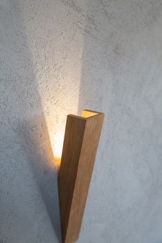 a light that is on the side of a wall next to a wooden pole with it's shadow